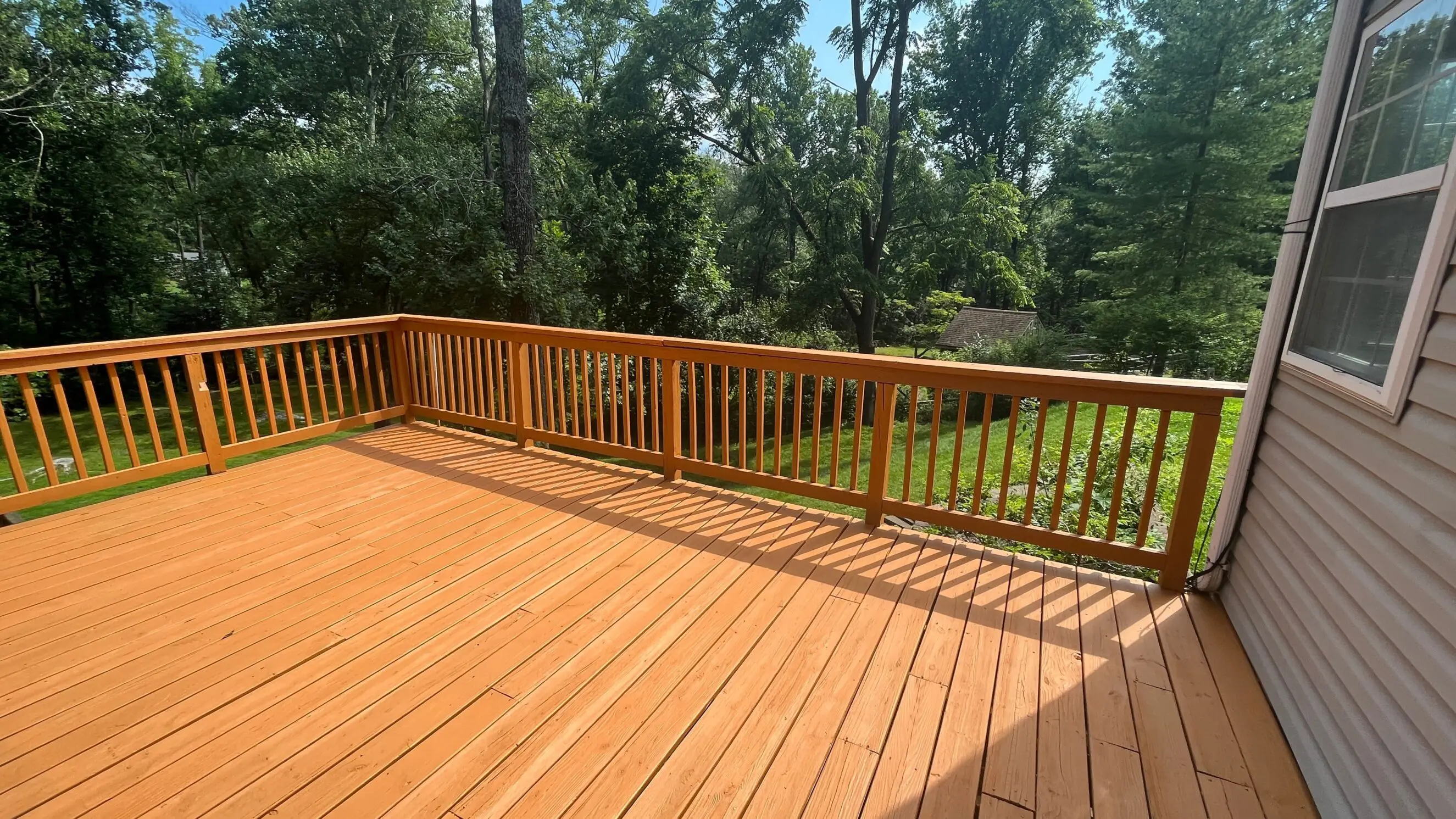 Newly built wooden deck with railing attached to a house, overlooking a green backyard with trees, showcasing custom decking solutions for outdoor living.