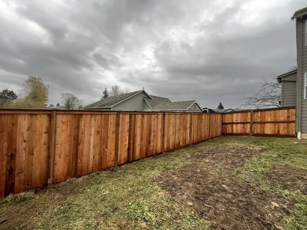 Newly installed cedar wood privacy fence enclosing a residential backyard under cloudy sky, showcasing Timberhill Fence & Deck quality craftsmanship.