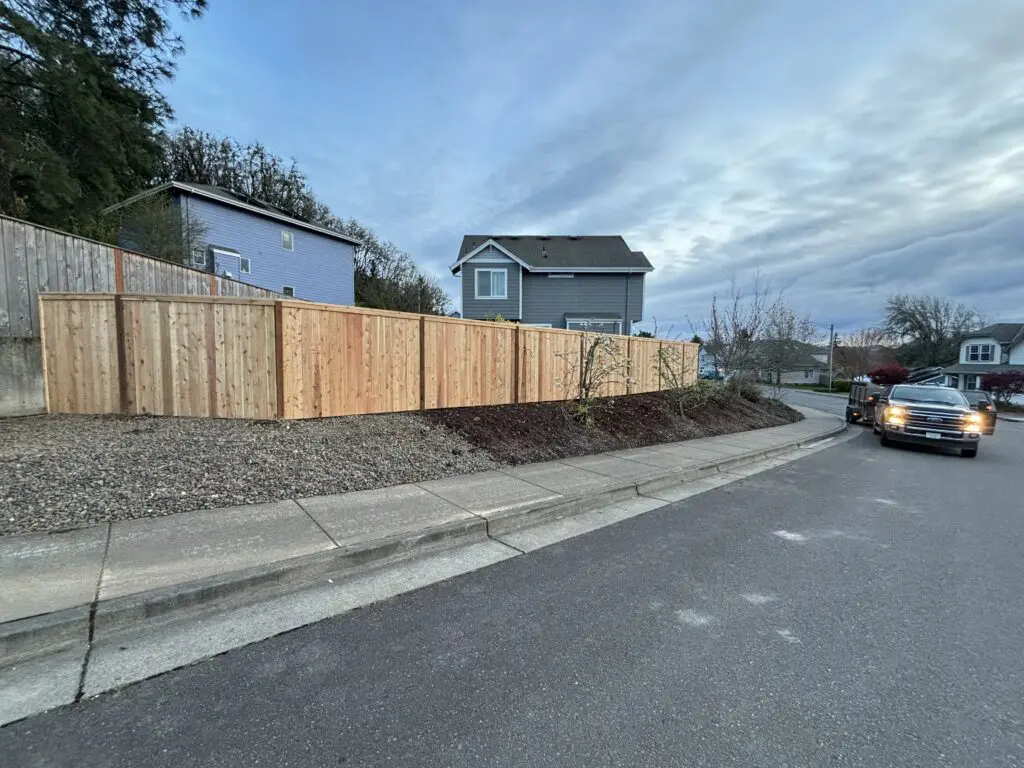 Newly installed cedar fence along residential sidewalk with landscaped mulch bed and nearby parked truck on Timberhill Fence & Deck project site.