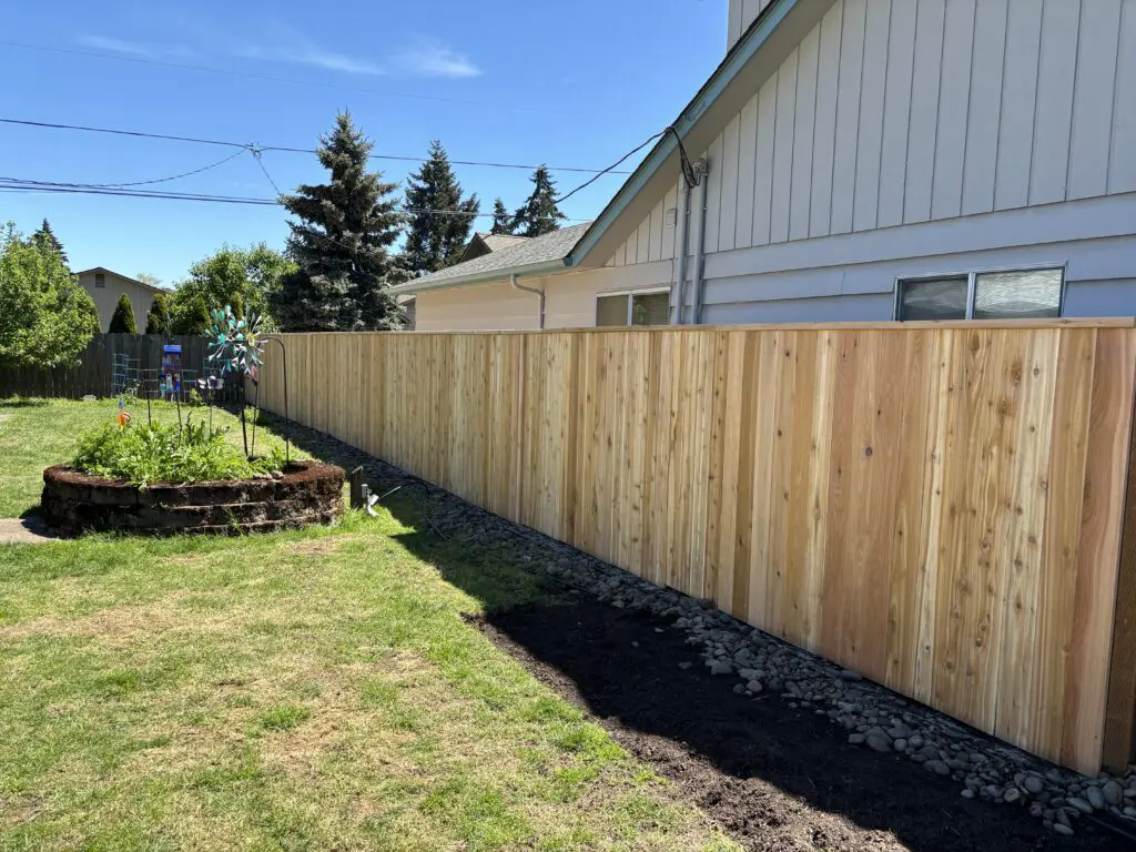 Newly installed wooden privacy fence along backyard of residential home with landscaped garden bed and clear blue sky, showcasing Timberhill Fence & Deck craftsmanship.