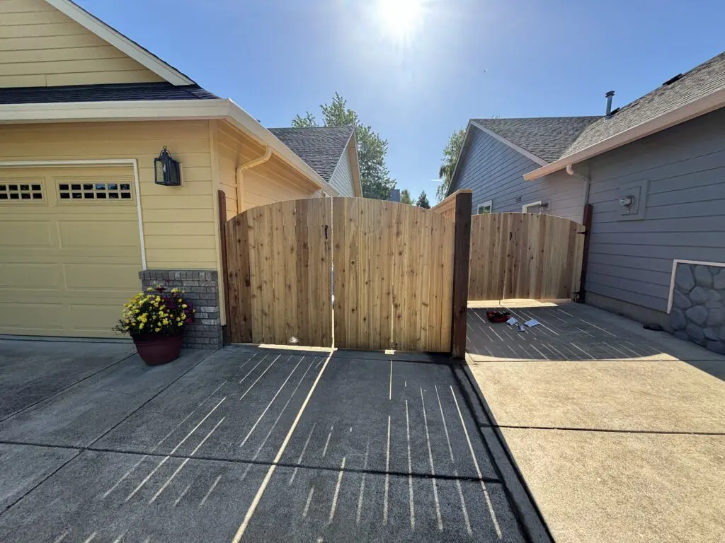 Double wooden driveway gates installed between two houses on a sunny day, showcasing Timberhill Fence & Deck's custom residential fence and gate solutions.