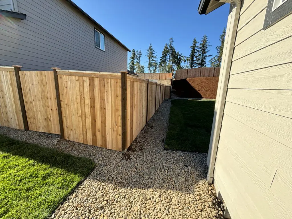 Newly installed wooden privacy fence with clean gravel pathway and fresh landscaping around residential homes under clear blue sky, showcasing Timberhill Fence & Deck quality craftsmanship.