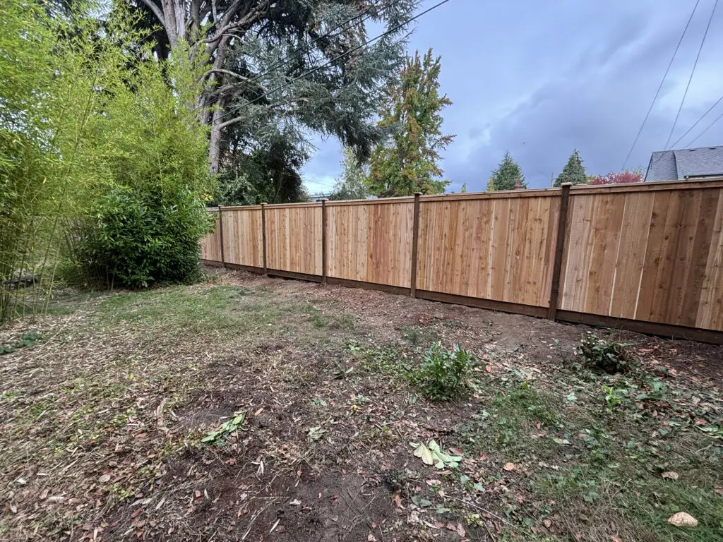 Newly installed wooden privacy fence enclosing a backyard area with sparse grass and surrounding trees, showcasing Timberhill Fence & Deck's residential fencing craftsmanship.